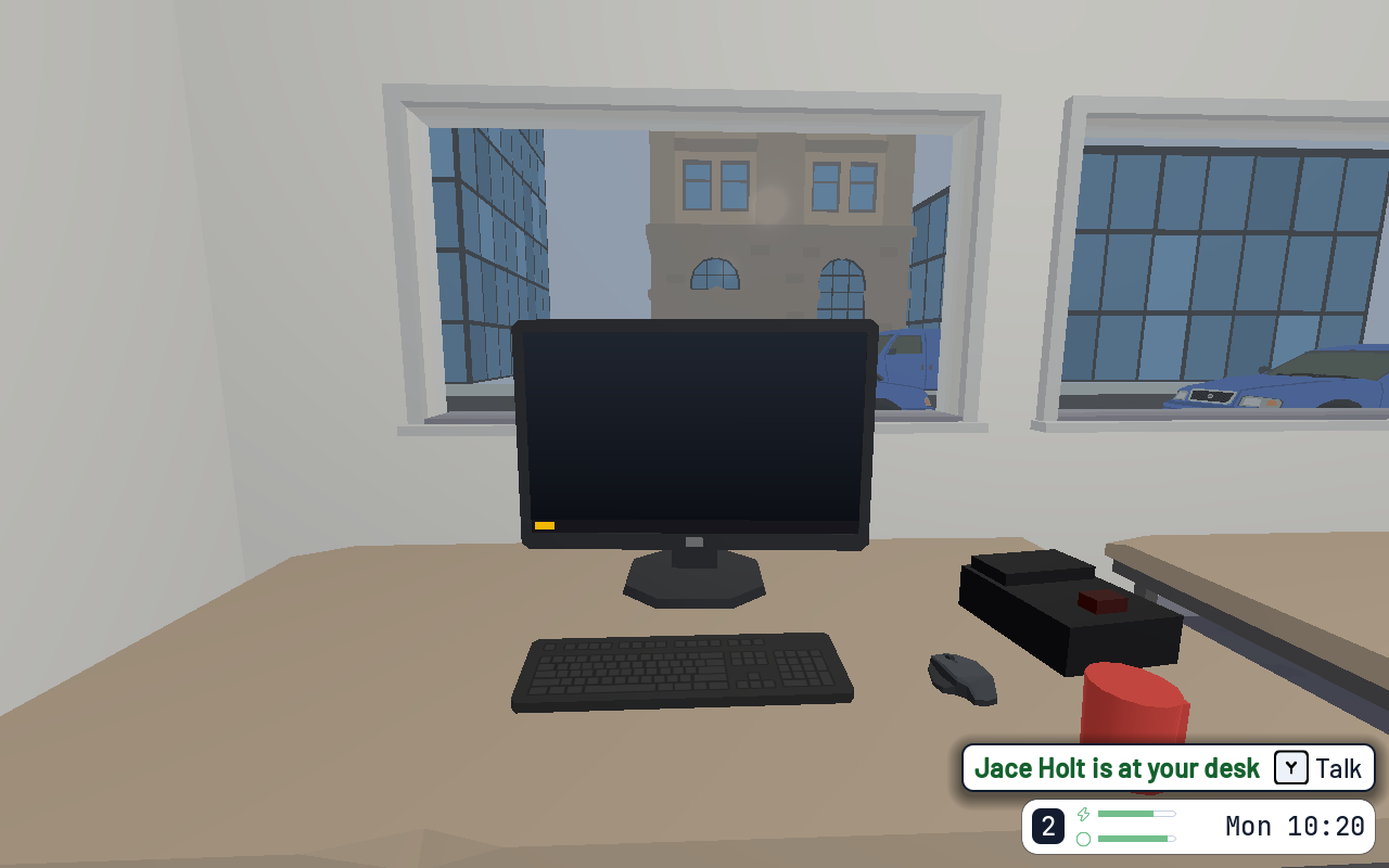 A first-person view of the intern's desk: a monitor, keyboard, mouse and red mug by a window onto the street, with a colleague waiting to talk.